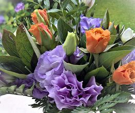 Bouquet con rose arancioni e fiori viola e verdi su sfondo di prato verde.