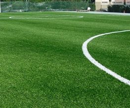 Kleines Fußballfeld mit grünem Kunstrasen und weißen Linien unter blauem Himmel.