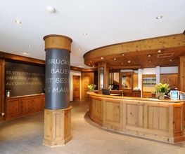 Holzgetäfelter Empfangsbereich eines Hotels mit Blumen und Schriftzug an der Säule.