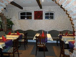 Gemütliches Restaurant mit gemusterten Stühlen, weißen Tischdecken und dekorativen rotem Rosenbild.