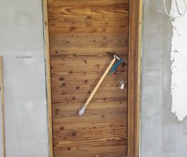 Holztür mit Besen, der schräg gegen die Tür lehnt, an einer unreparierten Wand.