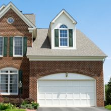 Brick house with green shutters and a two-car garage under a clear blue sky.