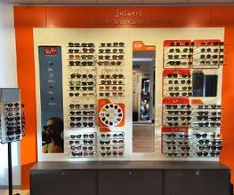 Zonnebrillenwand met diverse modellen in een winkel, tegen een oranje achtergrond.