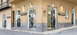 Negozio d'abbigliamento su un angolo di strada, con manichini nelle vetrine e insegne visibili.