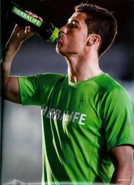 Hombre con camiseta verde bebe de una botella negra con la palabra "Herbalife".