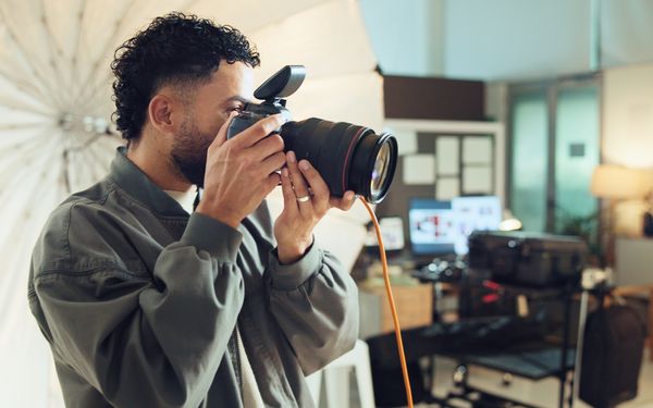 Ein Fotograf hält sich seine Kamera vor sein Gesicht, um Businessfotos von seiner Kundin für LinkedIn zu machen.