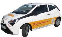 Weißes Auto mit gelber Reklame "Schnauzevollzeichen" an der Seite und QR-Code.