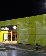 Entrada iluminada de supermercado Carrefour de noche con letrero que dice "Benvidos".