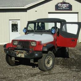 Red and gray off-road vehicle parked outside Bryan's auto shop with an open driver's door.
