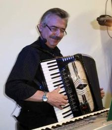 Mann mit schwarzem Hemd spielt Akkordeon und trägt ein Mikrofon.