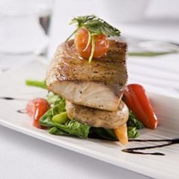 Gourmet fish dish with greens, cherry tomatoes, and garnish on a white plate.