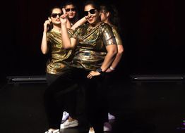 Four women in gold tops and sunglasses dancing confidently on stage.