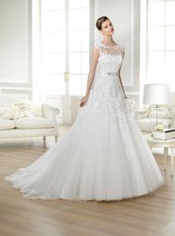 Braut in elegantem, weißem Kleid steht in einem hellen, stilvoll eingerichteten Wohnraum.