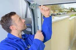 Man in blue uniform repairing a garage door with a screwdriver.