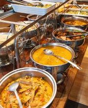 Buffet com variedade de pratos quentes e panelas de aço inoxidável.