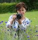 Frau in Blumenwiese mit Kamera, bereit zum Fotografieren.