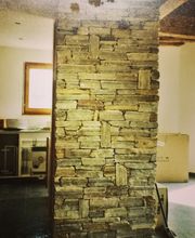 Steinwand in modernem Innenraum, links eine Küchenecke und rechts ein Karton im Hintergrund.