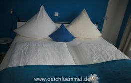 Ein Bett mit weißer Bettwäsche, blauen und weißen Kissen vor einer blauen Wand.