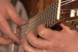 Nahaufnahme von Händen, die eine Gitarre spielen, mit Fokus auf die Saiten und Fingerpositionen.