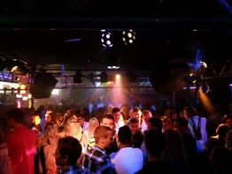 Menschen tanzen in einem dunklen Club, beleuchtet von bunten Lichtern und Scheinwerfern.