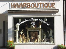 Schaufenster der Haarboutique mit Perücken und Dekorationen, darüber ein Schild "HAARBOUTIQUE".