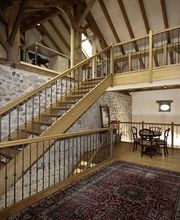 Holztreppe in einem Raum mit Steinwänden, Teppich und einem Tisch im Zwischengeschoss.