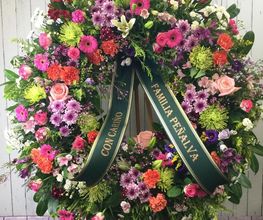 Corona floral colorida con cinta verde dedicada a "FAMILIA PEÑALVA".