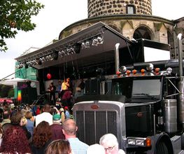 LKW-Bühne mit einer Band, die vor einer großen Menschenmenge bei einem Freiluftkonzert spielt.