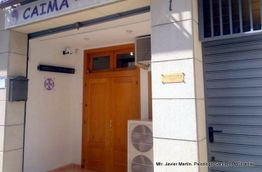 Entrada de oficina, puerta de madera, aire acondicionado y cartel dorado en la pared.