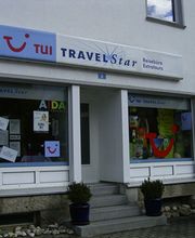 Fassade eines Reisebüros mit Schaufenstern voller Poster, Schilder und Pflanzen auf Stufen.