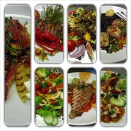 Verschiedene Teller mit Fisch, Fleisch, Salaten und gegrilltem Gemüse, kunstvoll angerichtet.