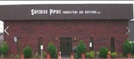 Brick building with "Superior Piping" sign, surrounded by potted plants and greenery.