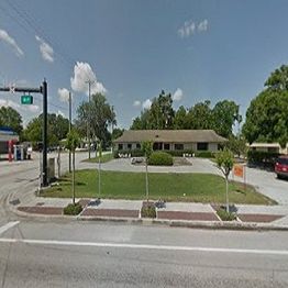 Street view of a single-story building with surrounding greenery and a gas station nearby.