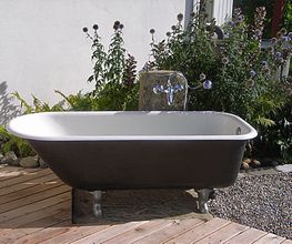 Freistehende Badewanne im Freien, umgeben von Pflanzen und Kiesweg.
