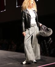 Eine Frau auf dem Laufsteg mit Lederjacke und karierter Hose hält eine Winterjacke.