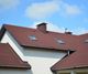 Red shingle roof with skylights and chimney against a blue sky.
