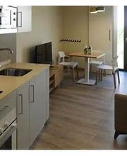 Sala moderna con cocina integrada, sofá, mesa de comedor, televisor y balcón con puertas de vidrio.