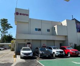 Edificio blanco con logo "Evonik" y cinco autos estacionados al frente en un día soleado.