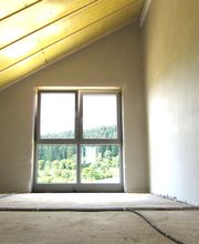 Dachzimmer mit Fenster, Blick auf bewaldete Landschaft, unvollendeter Boden.