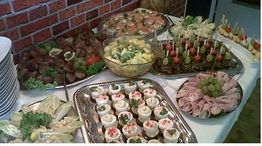 Tisch mit vielseitigem Buffet: belegte Brötchen, Fleisch, Obst und Gemüse auf Silbertabletts.