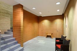 Holzwand-Flur mit Treppen, zwei Türen und Stühlen; warme Beleuchtung.