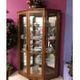 Wooden corner cabinet with glass doors displaying plates and glassware against a pink wall.