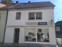 Zweistöckiges Haus mit Allianz-Büro, Schaufenster, Herzvorhängen und benachbarten Gebäuden.