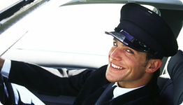 Smiling chauffeur in uniform sitting in a car, facing the camera.