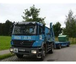 Blauer Lastwagen mit Hänger parkt auf einer ländlichen Straße, umgeben von Bäumen.