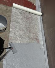 Rodillo aplicando pintura en una superficie cubierta con tela. Cubeta al lado izquierdo.