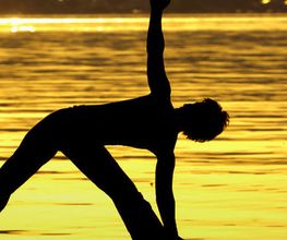 Ein Mensch macht eine Yoga-Pose am Strand bei Sonnenuntergang.