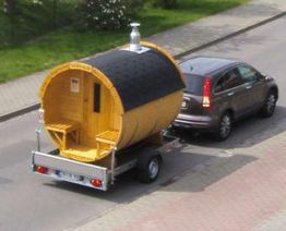 Auto zieht eine fassförmige Sauna auf einem Anhänger die Straße entlang.