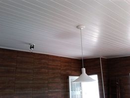 Teto com forro branco, luminária pendente e parede de madeira escura ao fundo.