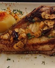 Pescado asado con ajo en rodajas y papa hervida espolvoreada con pimentón, servido en un plato blanco.